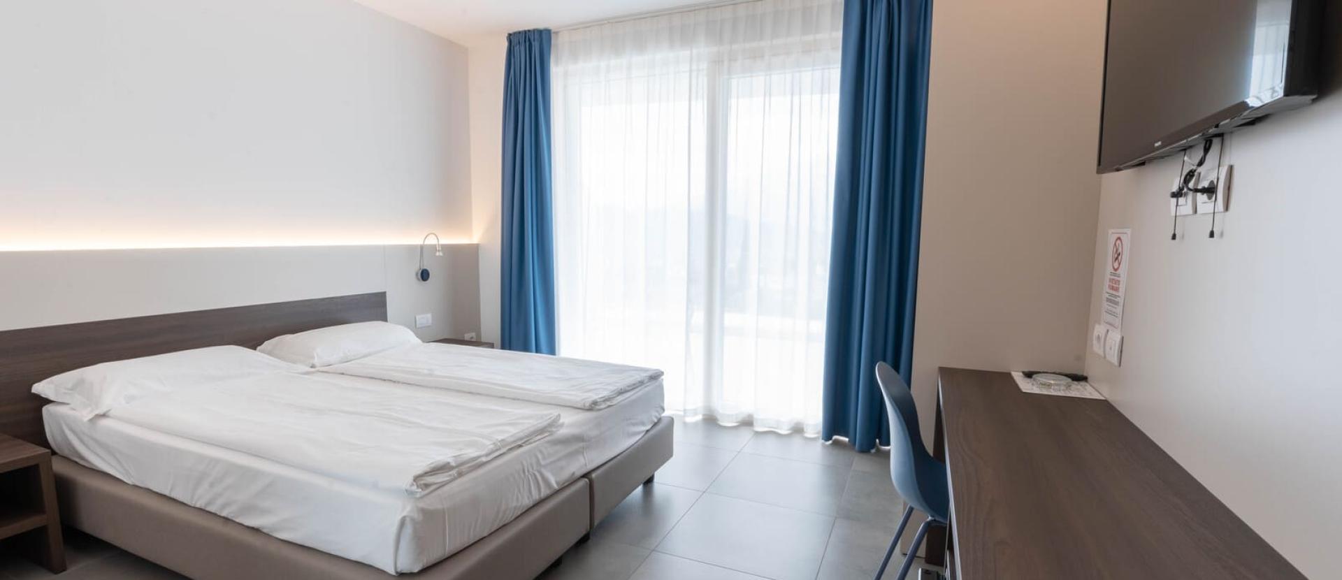 Camera moderna e luminosa, con letto matrimoniale e tende blu, atmosfera rilassante.