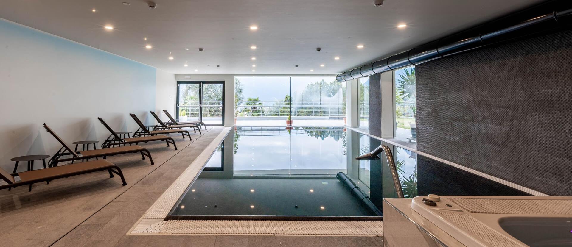 Piscina interna elegante con lettini, atmosfera rilassante e vista su giardino verde.