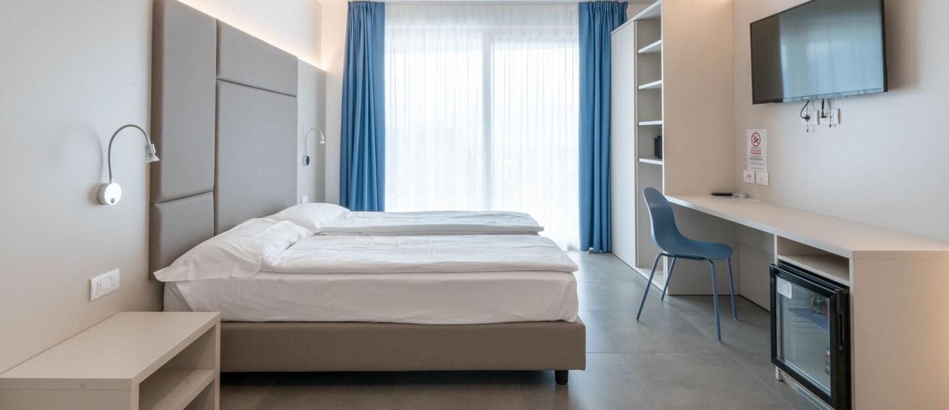 Camera moderna e luminosa con letti gemelli, tende blu e arredi minimalisti.