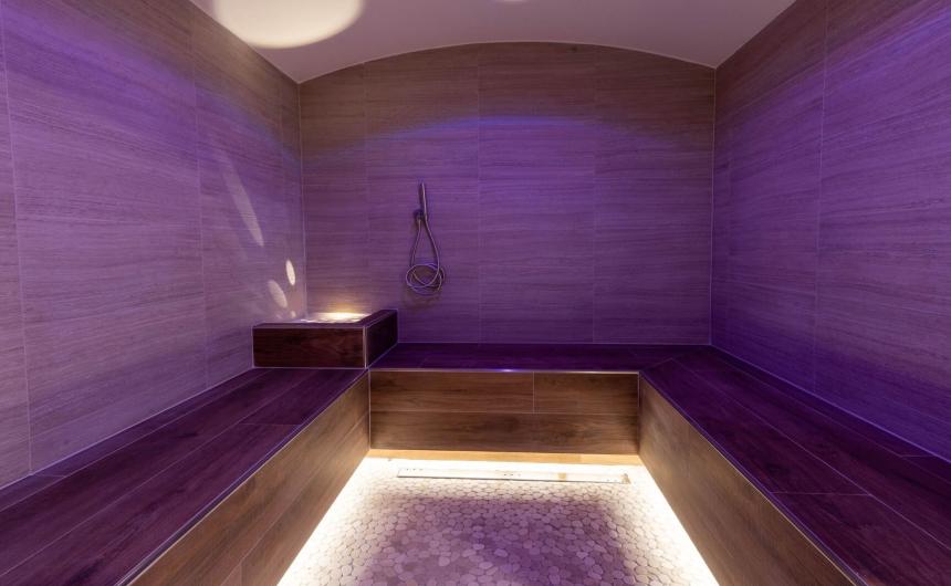 Bagno turco con luci soffuse viola, atmosfera rilassante e calda, perfetta per il relax.