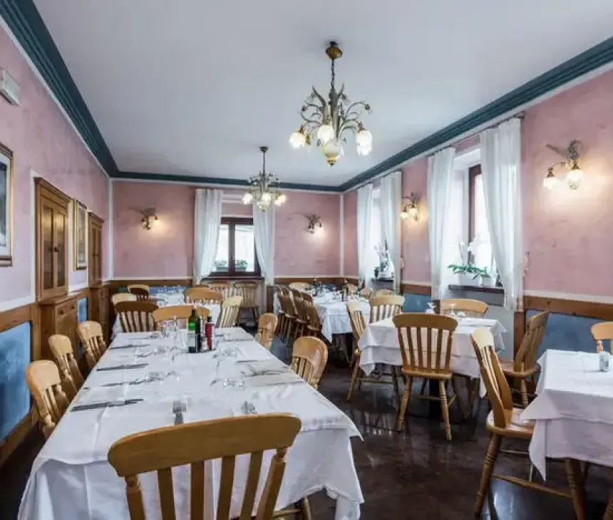 Ristorante accogliente, tavoli apparecchiati, sedie in legno, pareti rosa, atmosfera calda e luminosa.