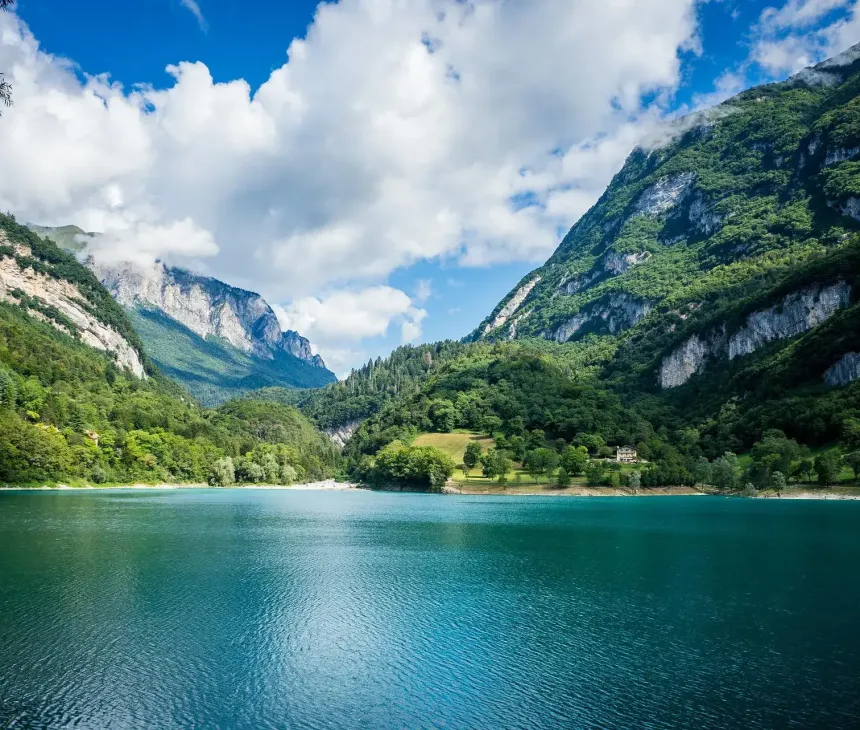 Lago alpino sereno, montagne verdi, cielo azzurro e nuvole soffici, pace e bellezza naturale.