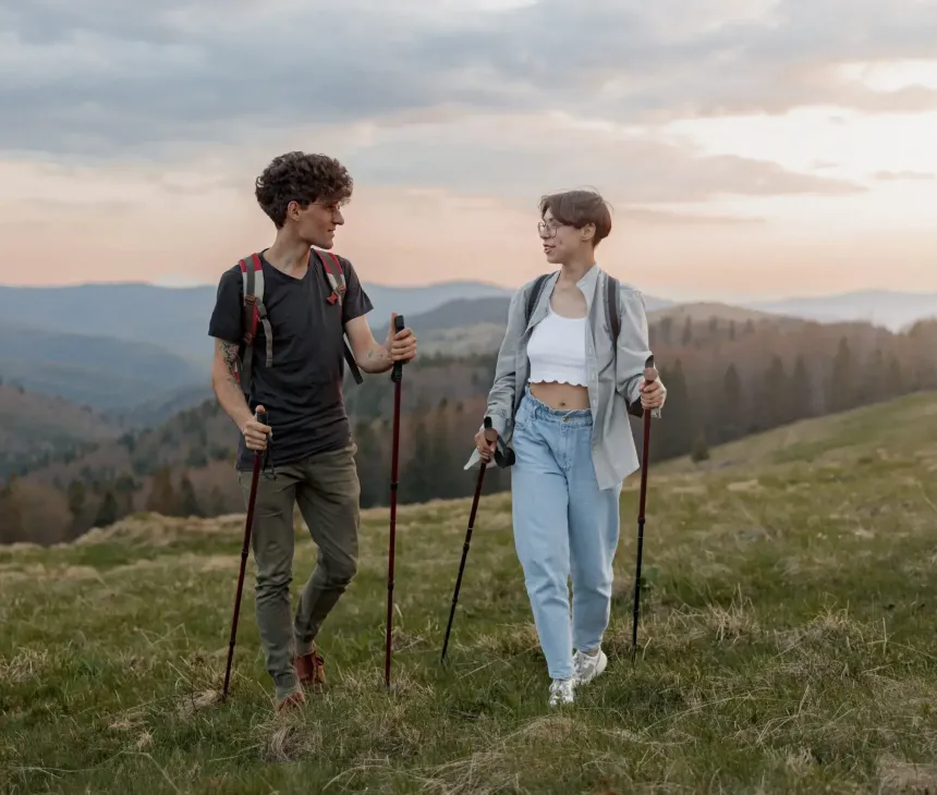Due persone sorridenti fanno trekking in montagna al tramonto, immersi nella natura.