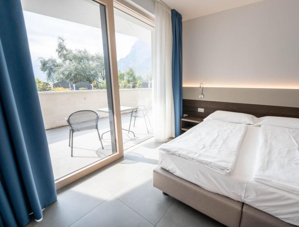 Camera luminosa, letto comodo, vista montagna, terrazza accogliente con sedie, atmosfera rilassante.