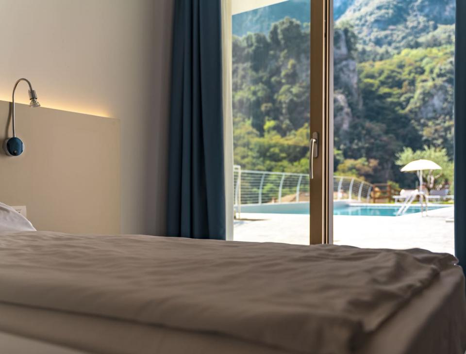 Camera luminosa con vista su piscina e montagne, atmosfera rilassante e serena.