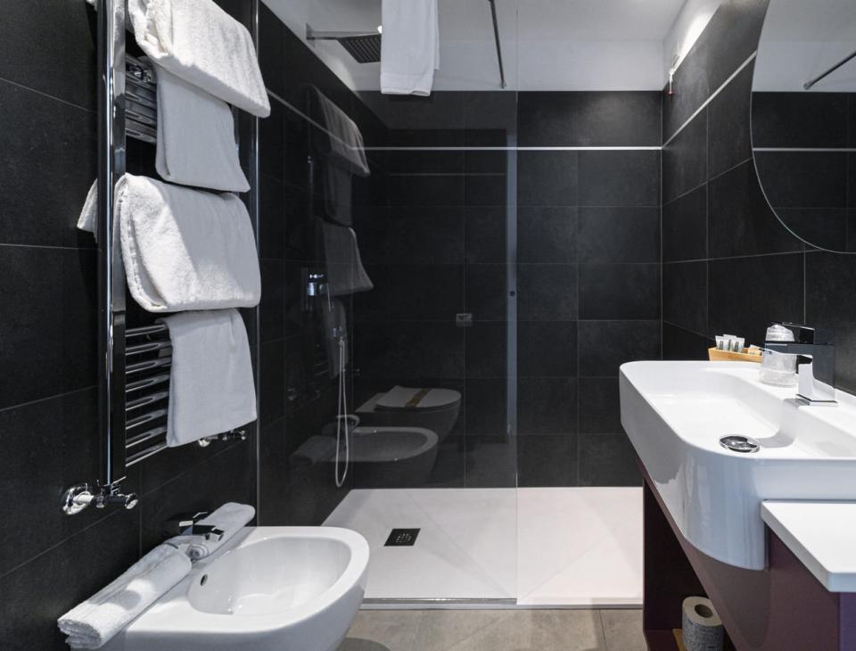 Bagno moderno, elegante, con pareti scure, doccia spaziosa e asciugamani bianchi soffici.