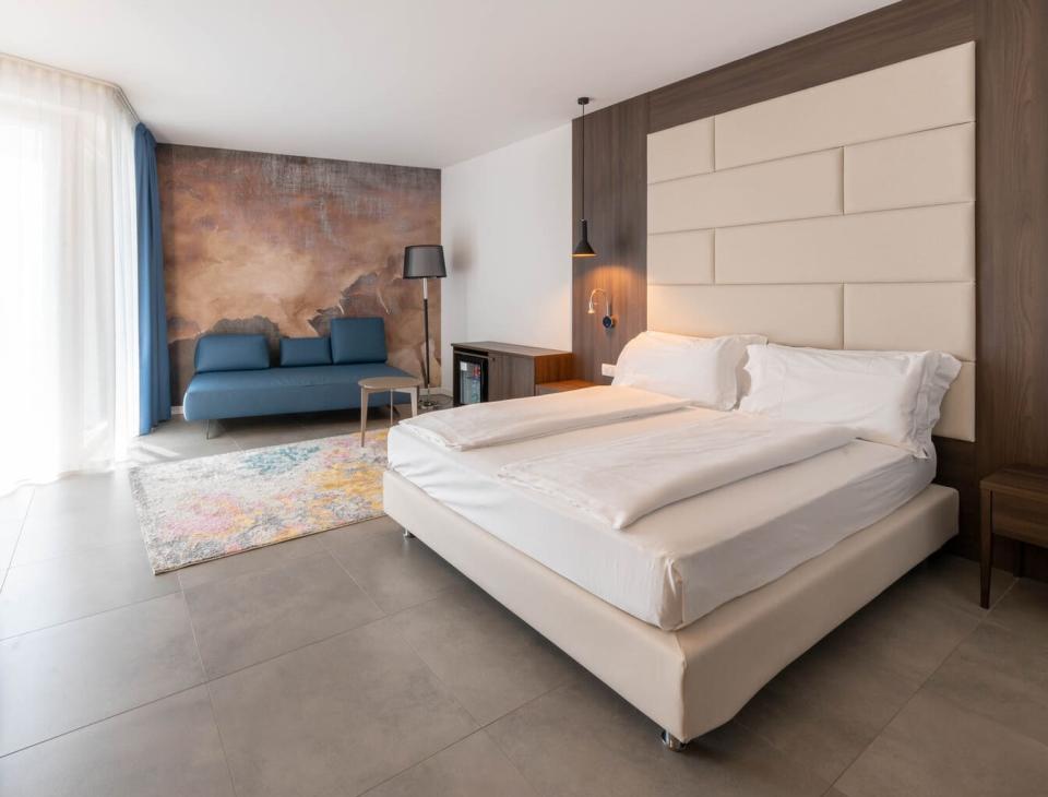 Camera moderna, luminosa, con letto accogliente, divano blu e parete artistica.