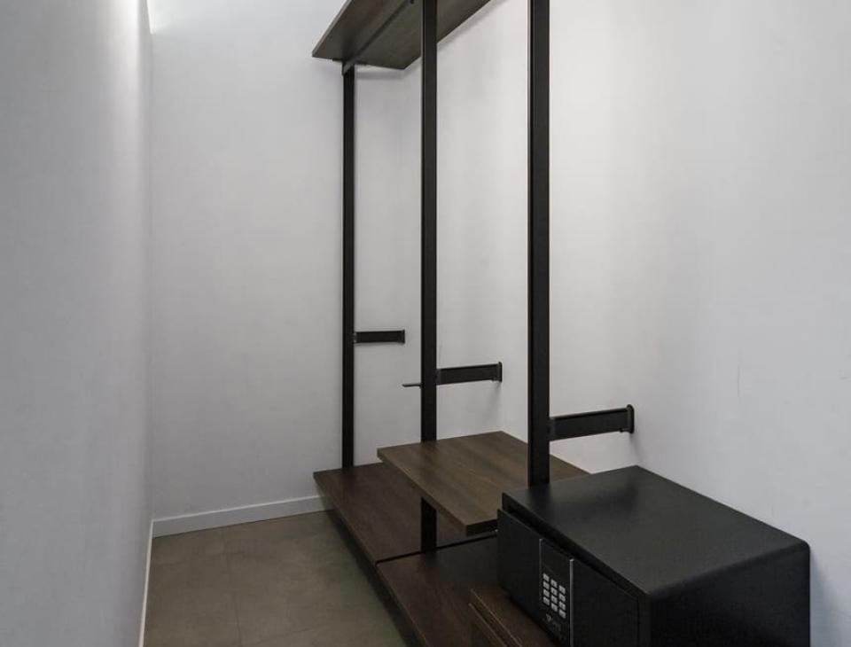 Stanza stretta, scaffali scuri, cassaforte sicura, atmosfera minimale e ordinata.
