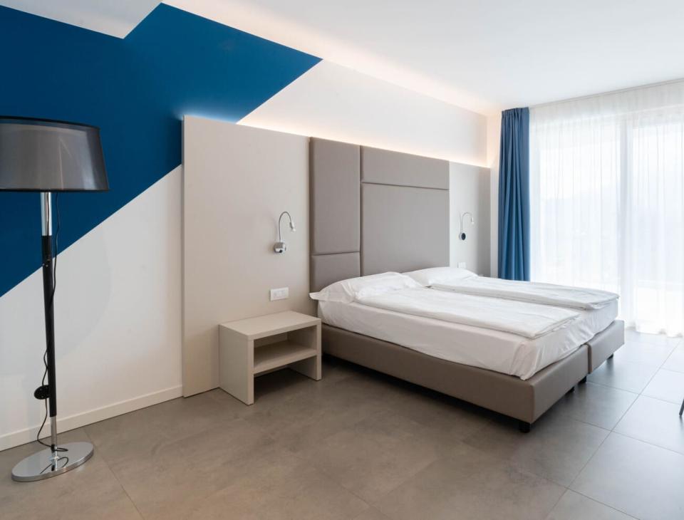 Camera moderna, luminosa, con letto matrimoniale, pareti bianche e blu, atmosfera minimalista.