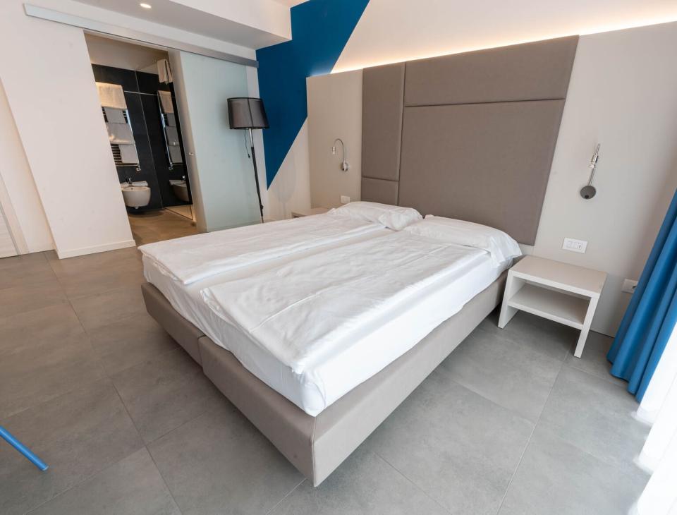 Camera moderna, minimalista, con letto matrimoniale, tonalità blu e grigio, atmosfera rilassante.
