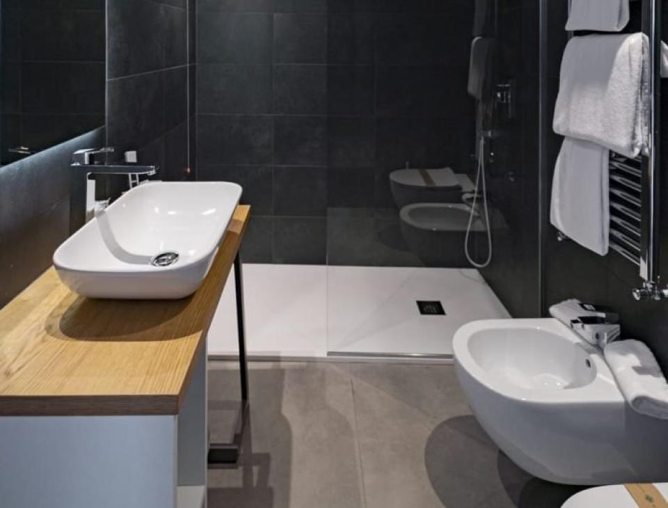 Elegante bagno moderno con piastrelle scure, lavabo bianco e doccia spaziosa.
