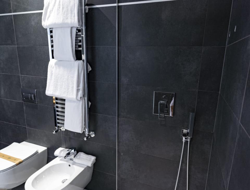 Elegante bagno moderno con doccia a pioggia, bidet e asciugamani bianchi su sfondo scuro.